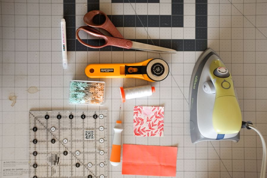 quilting tools including an iron, fabric, rotary cutter, quilting ruler, and cutting mat